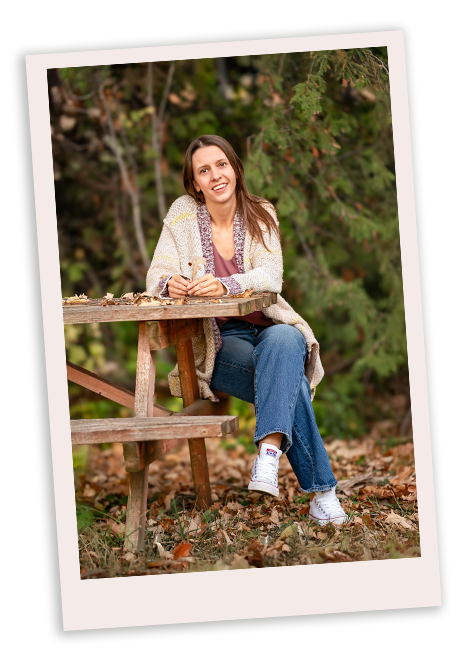 Erin Erin sits on the edge of a picnic table, legs crossed, looking at the camera. She is holding a leaf in her hand.