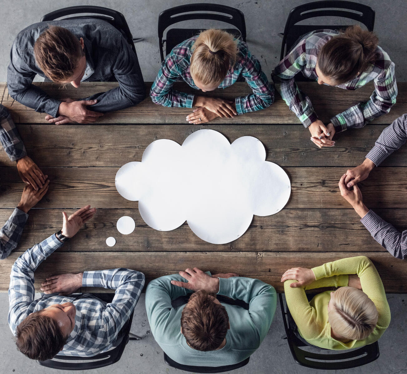 Career Support for Workplaces Career Support for Workplaces - Six individuals, with the hands of two more, sit at a wooden table with a gigantic thought cloud on it.
